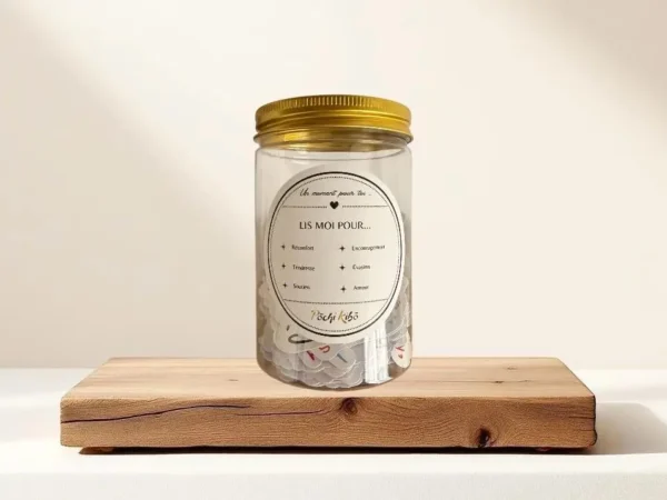 Bocal Mood Pills Pochi Kibo vu de face, avec une étiquette 'Lis-moi pour…', contenant de petits mots de réconfort, d’encouragement, de soutien, d’évasion, de tristesse et d’amour, posé sur un morceau de bois sur une table avec un fond beige